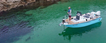 Pescador en una embarcación azul utilizando un motor eléctrico de proa Watersnake Geo-Spot GPS desplegado para mantener la posición en aguas cristalinas junto a la costa rocosa.