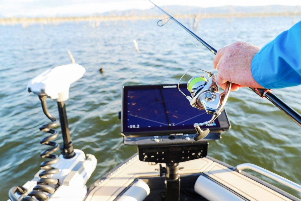 Pescador sosteniendo una caña frente a una sonda GPS plotter Lowrance y un motor eléctrico alimentados por una batería de litio LiFePO4 PoweryMax TX.