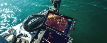 Vista desde la proa de una embarcación de pesca mostrando dos pantallas Lowrance operando en tiempo real con el sonar ActiveTarget 2 XL. En las pantallas se aprecian vistas detalladas del fondo y un árbol sumergido, junto al motor eléctrico desplegado en el agua.