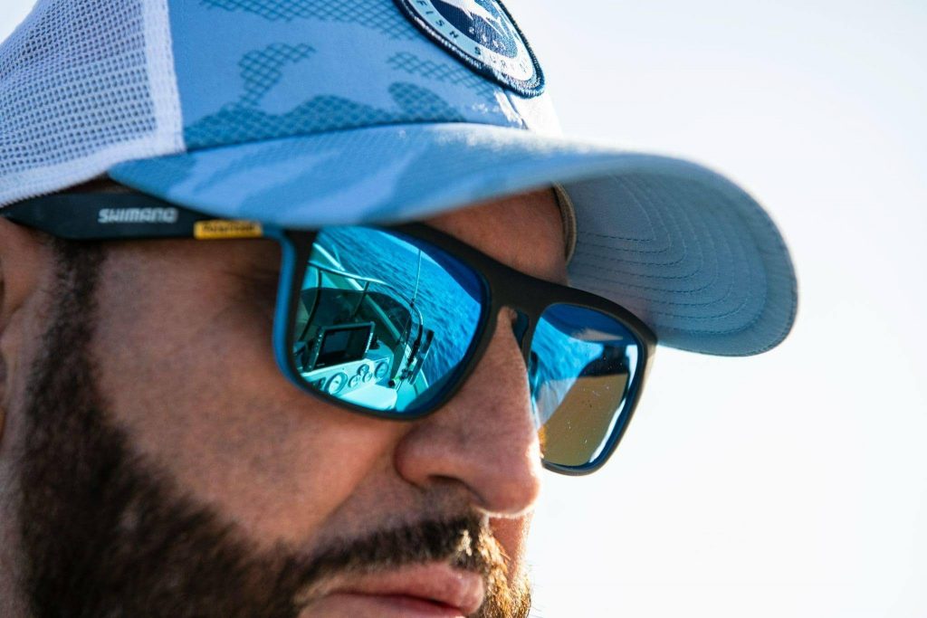 Pescador equipandose con gafas de sol polarizadas Shimano y gorra para proteccion solar en embarcacion