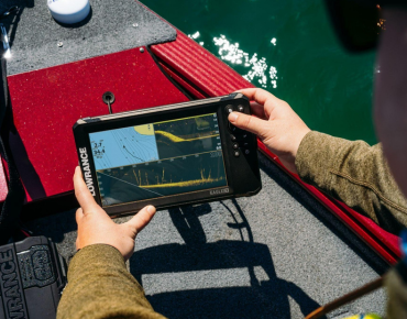 Pescador interactuando con la sonda GPS plotter Lowrance Eagle Eye 9 en tiempo real, a bordo de un barco, visualizando datos de sonda y cartografía.