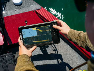 Pescador interactuando con la sonda GPS plotter Lowrance Eagle Eye 9 en tiempo real, a bordo de un barco, visualizando datos de sonda y cartografía.